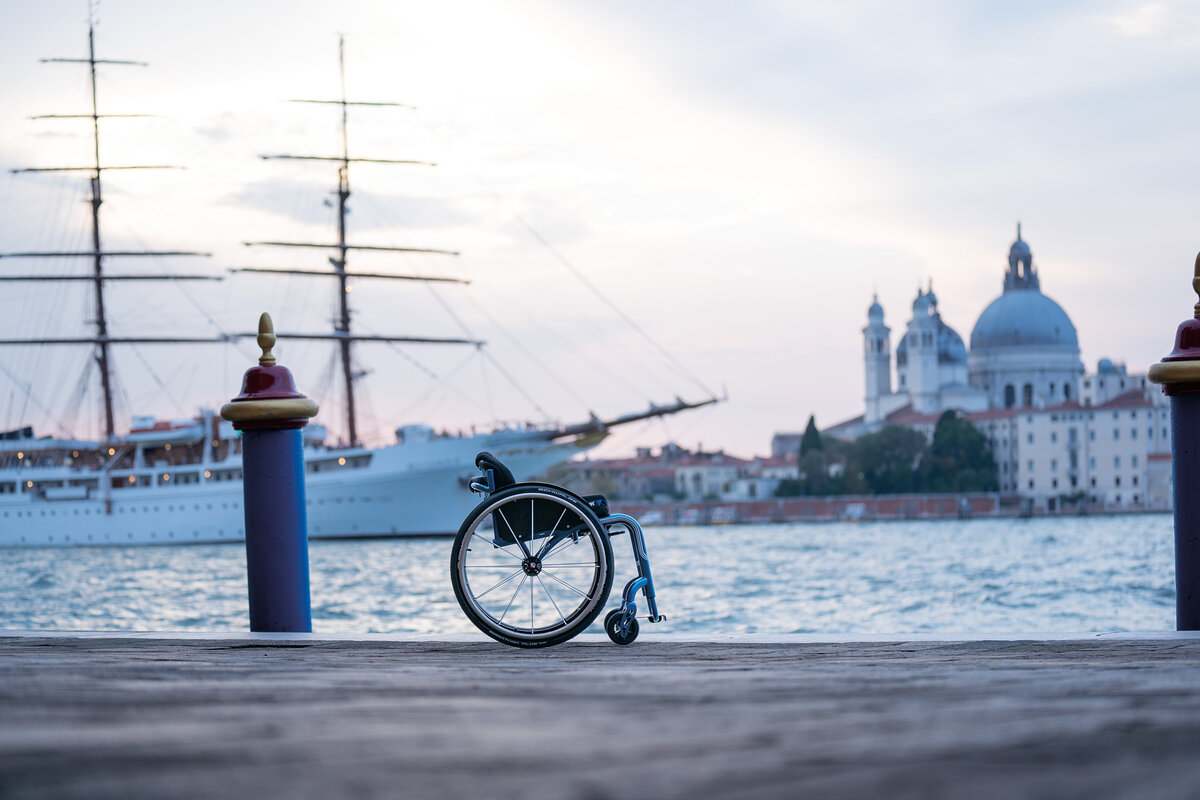 Una carrozzina OFFCARR sulla riva a Venezia, con un veliero e la Salute sullo sfondo